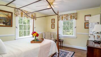 A bedroom with a four-poster bed, a chandelier, and a view of the outdoors through large windows.