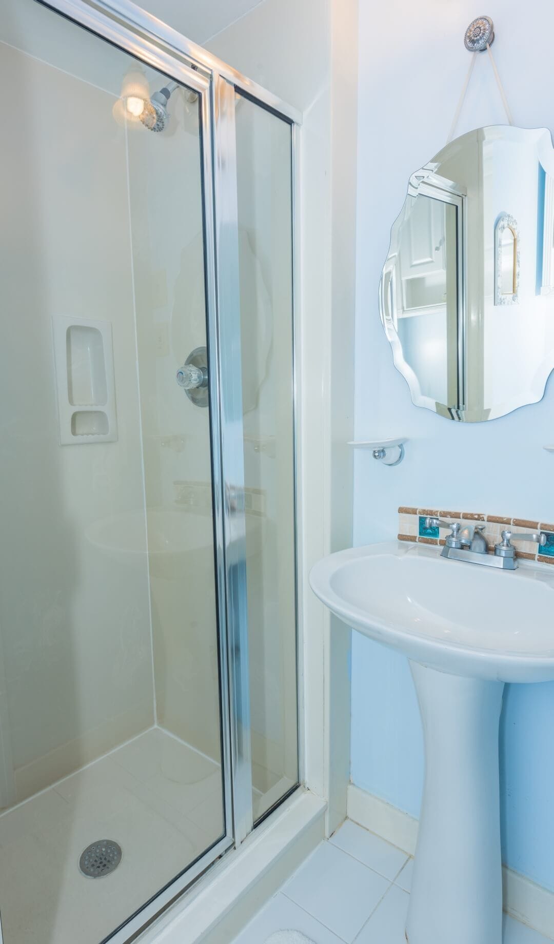 A modern bathroom with a glass-enclosed shower, a white sink, and a mirror with a decorative frame.