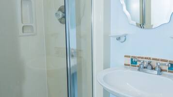 A modern bathroom with a glass-enclosed shower, a white sink, and a mirror with a decorative frame.