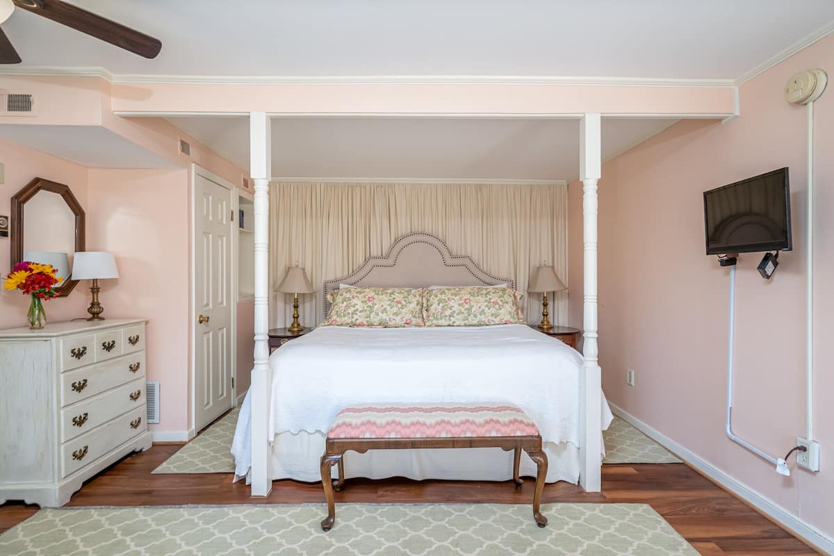 Une chambre à coucher avec un lit à baldaquin, une table de chevet avec des lampes, une commode et un téléviseur fixé au mur.