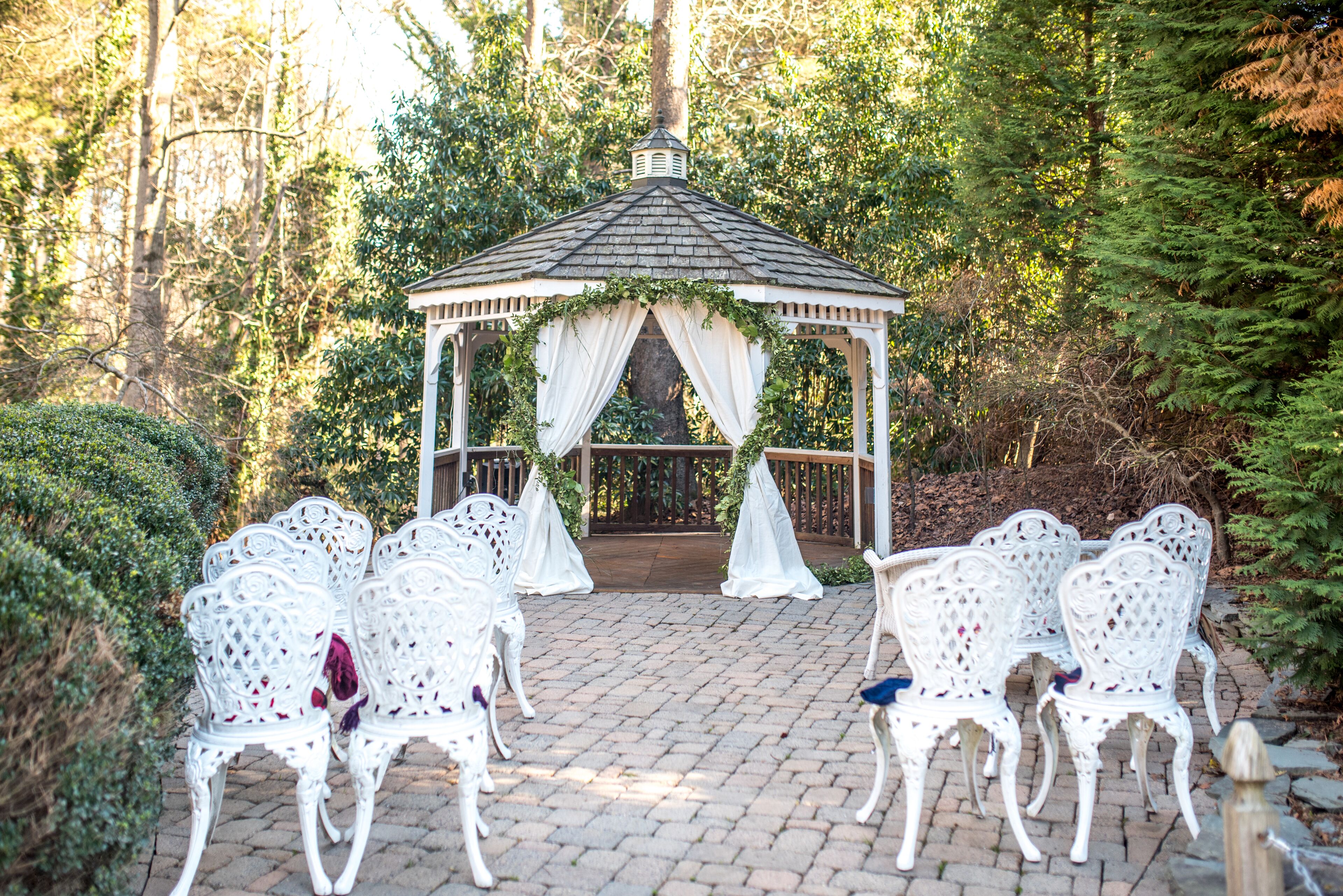 A gazebo with white chairs arranged in front, surrounded by greenery.