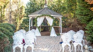 A gazebo with white chairs arranged in front, surrounded by greenery.