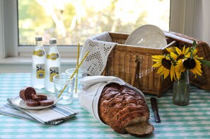 A table with a loaf of bread, a plate of sliced sausage, a glass of water, and a vase with sunflowers.
