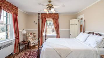A bedroom with a four-poster bed, a wooden chair, a small table, and a window with curtains.