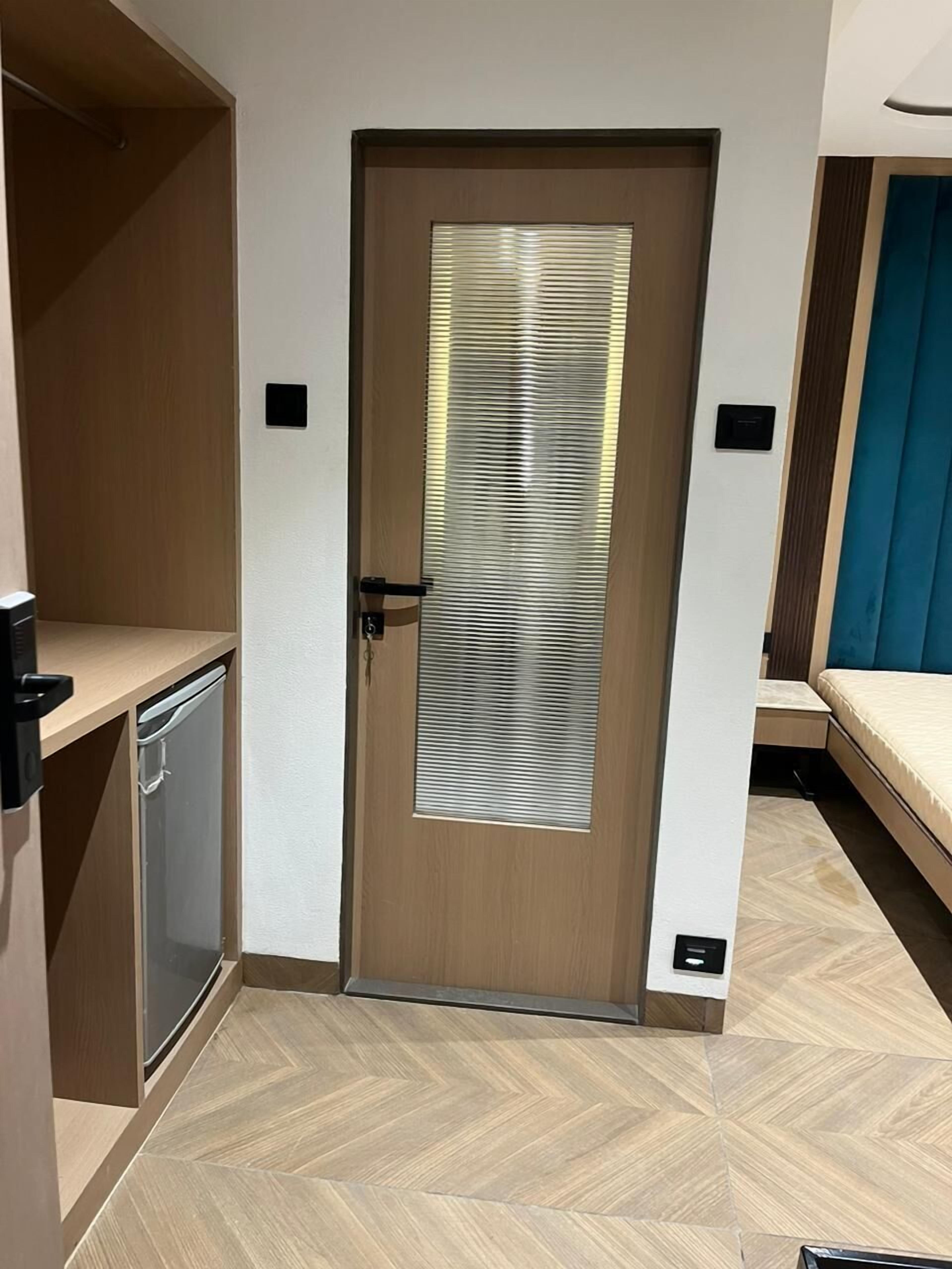 A compact room with a wooden door, a small kitchenette, and a bed with a blue headboard.