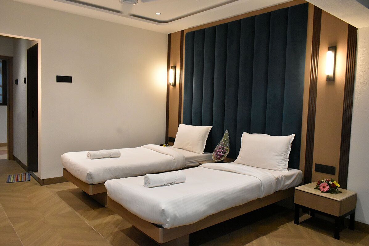 Habitación de hotel con dos camas individuales, cabecera oscura, lámparas de noche y una mesita de noche con un arreglo floral.