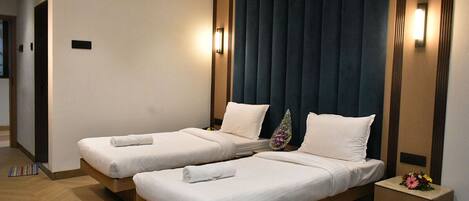 Habitación de hotel con dos camas individuales, cabecera oscura, lámparas de noche y una mesita de noche con un arreglo floral.