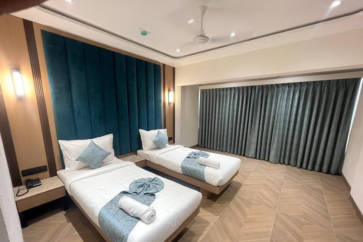 Habitación de hotel con dos camas, ventilador de techo y una ventana grande con cortinas.