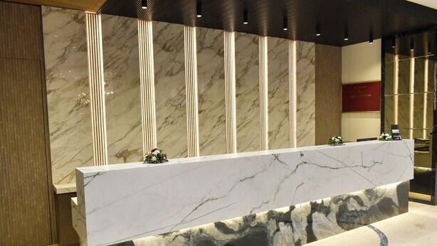 A reception desk with a marble top and vertical light strips, set against a marble wall with a plaque. - Hotel Supreme (Vasco) (Vasco da Gama)
