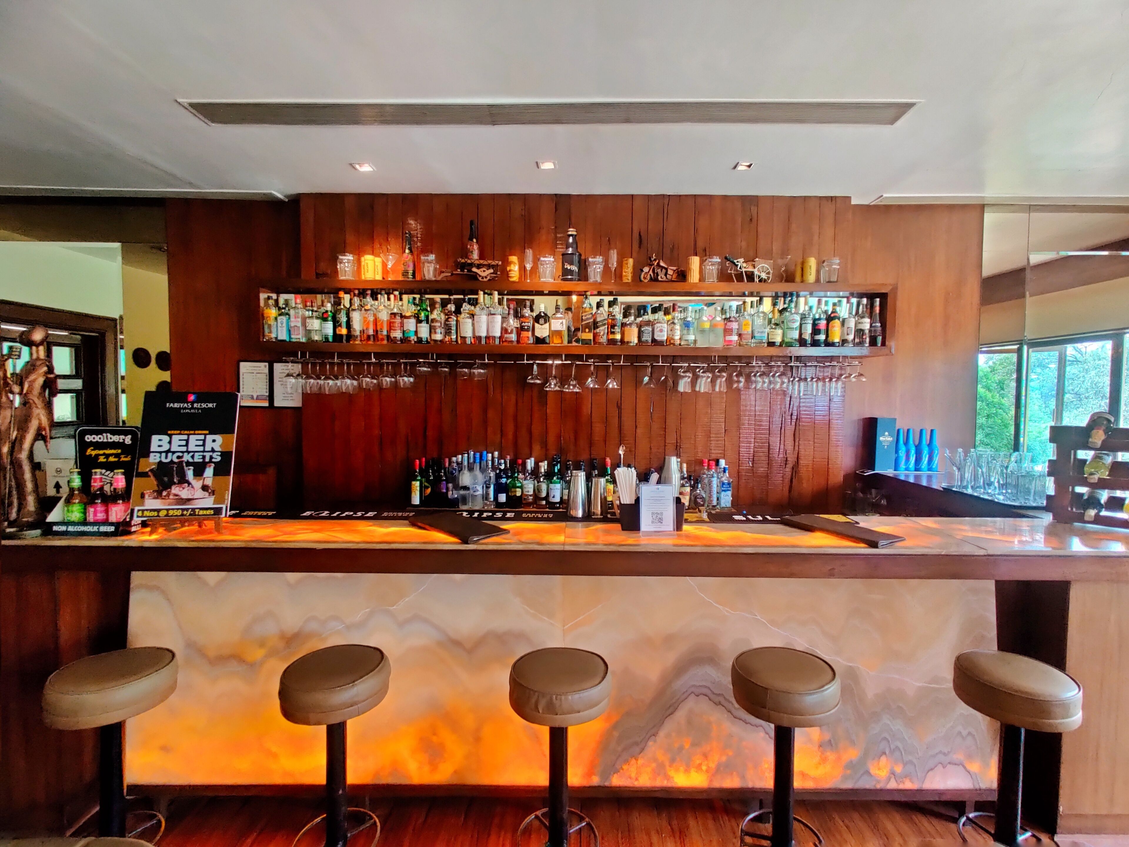 A bar area with a wooden counter, multiple liquor bottles, glasses, and stools.
