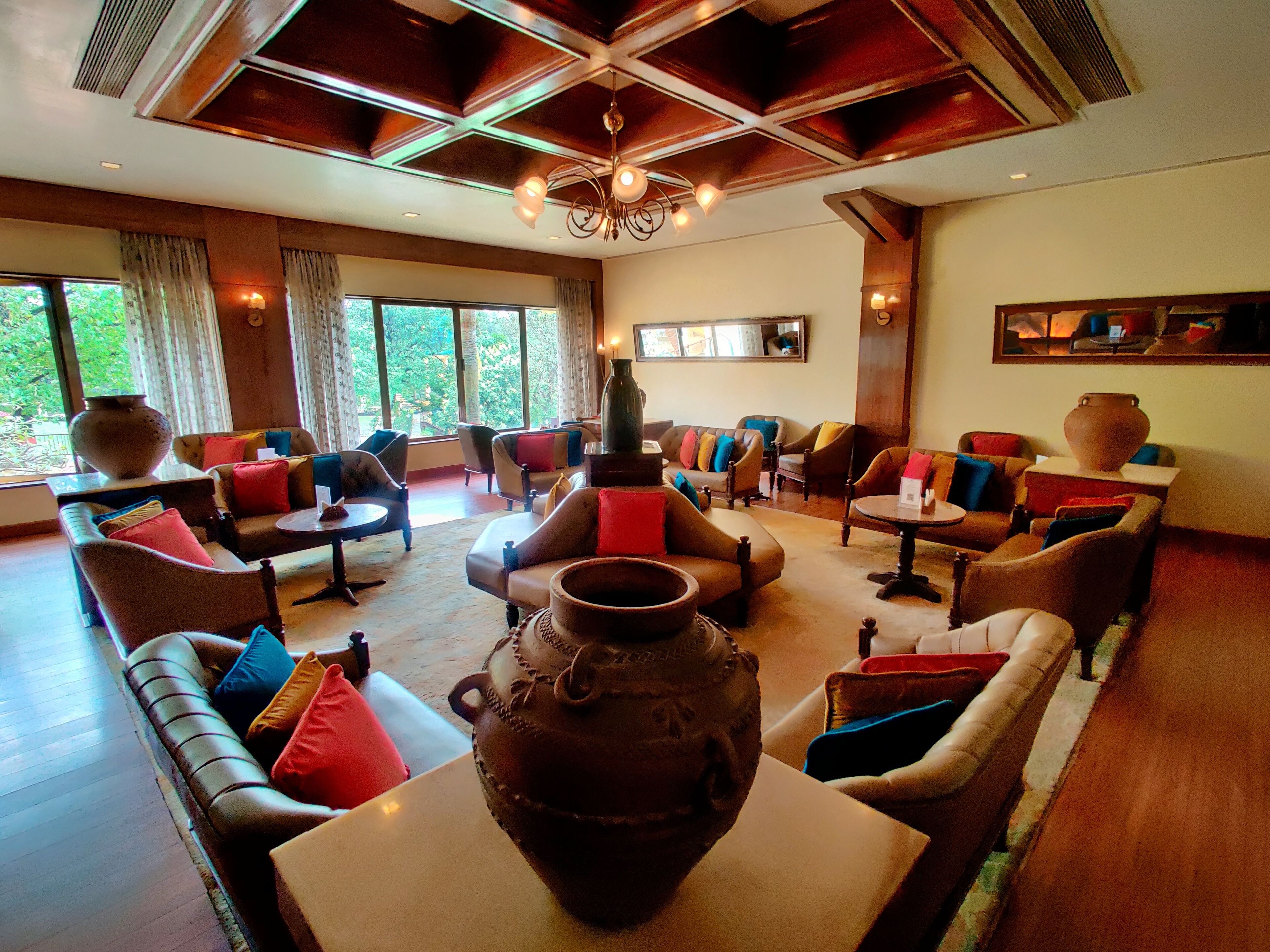 A spacious lounge area with multiple seating options, including sofas and armchairs, arranged around a central coffee table. There are large windows providing a view of the outdoors.