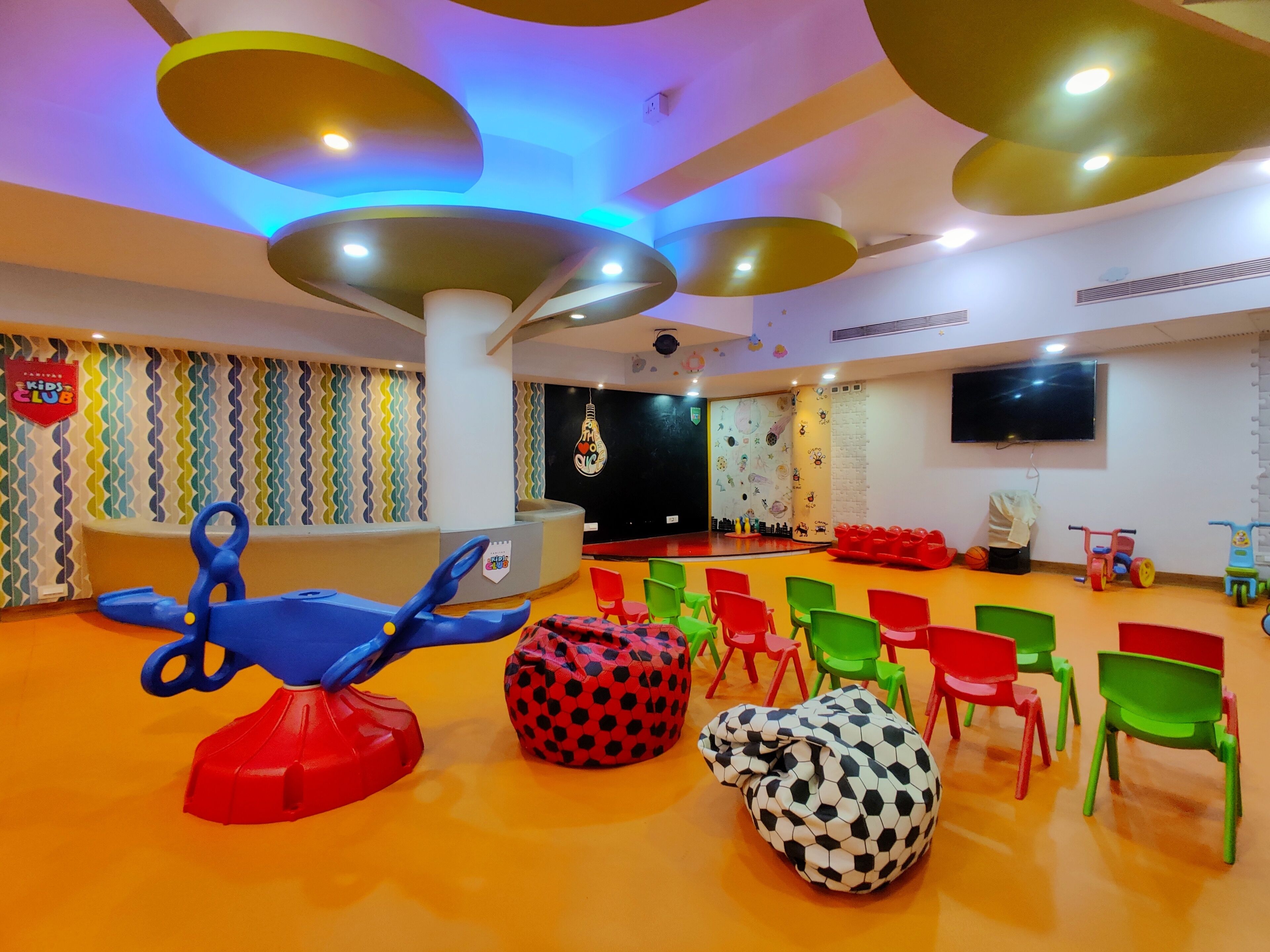 Uma área de recreação infantil com cadeiras coloridas, puffs e um barco de brinquedo azul.