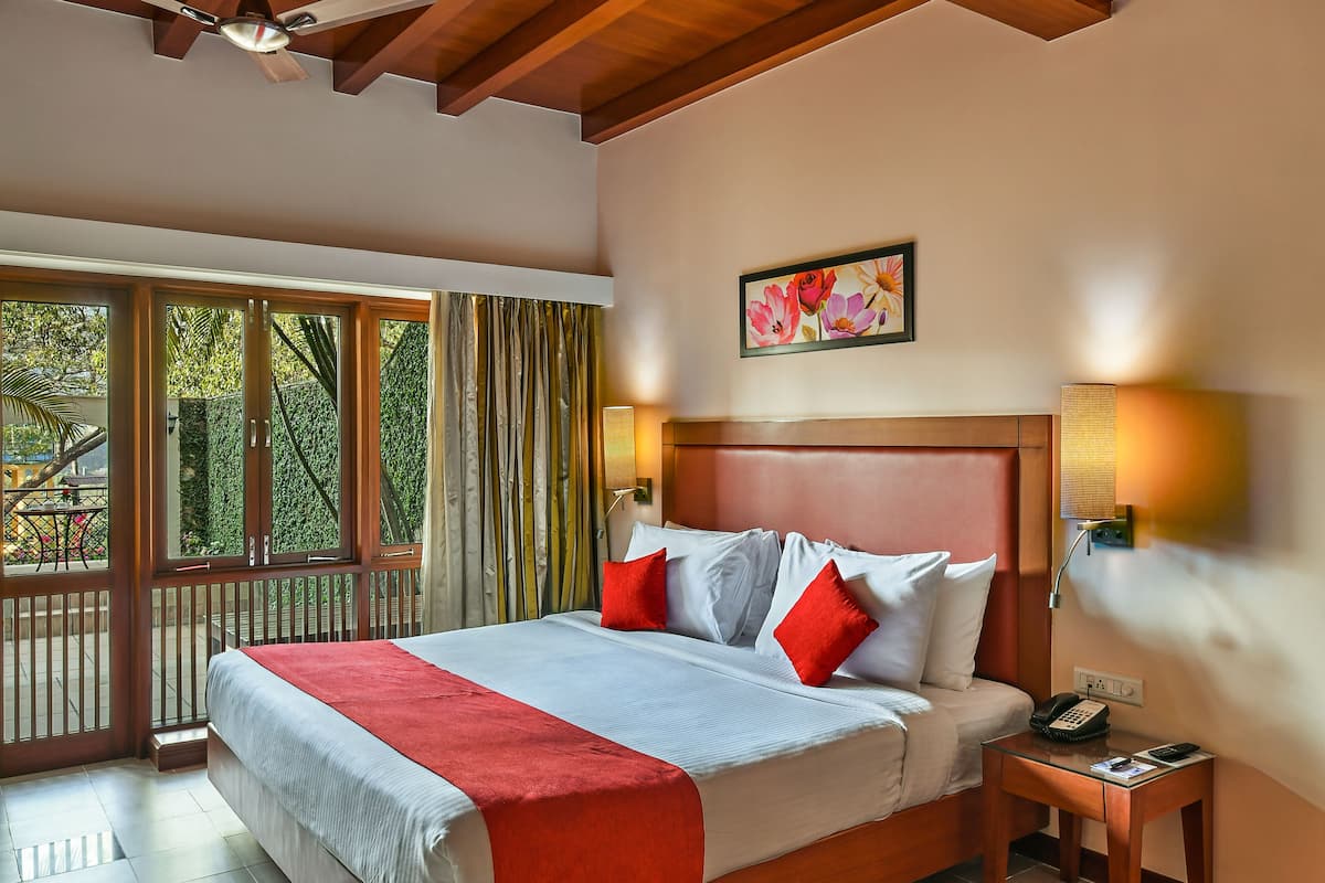 A bedroom with a wooden ceiling, a large bed with red and white bedding, a nightstand with a phone, and a window with curtains.