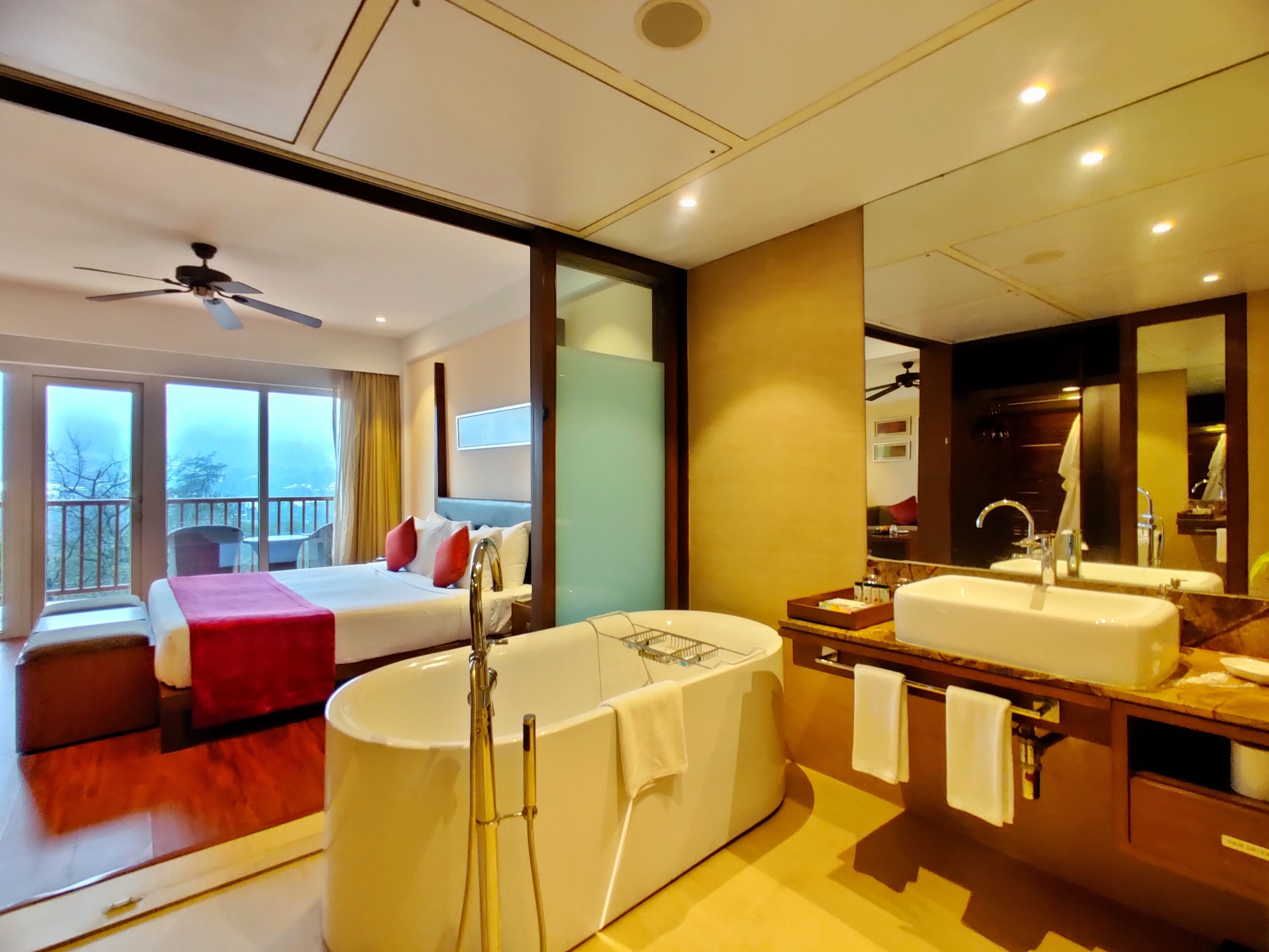 A hotel room with a large bed, a separate bathroom with a bathtub, and a balcony with a view.