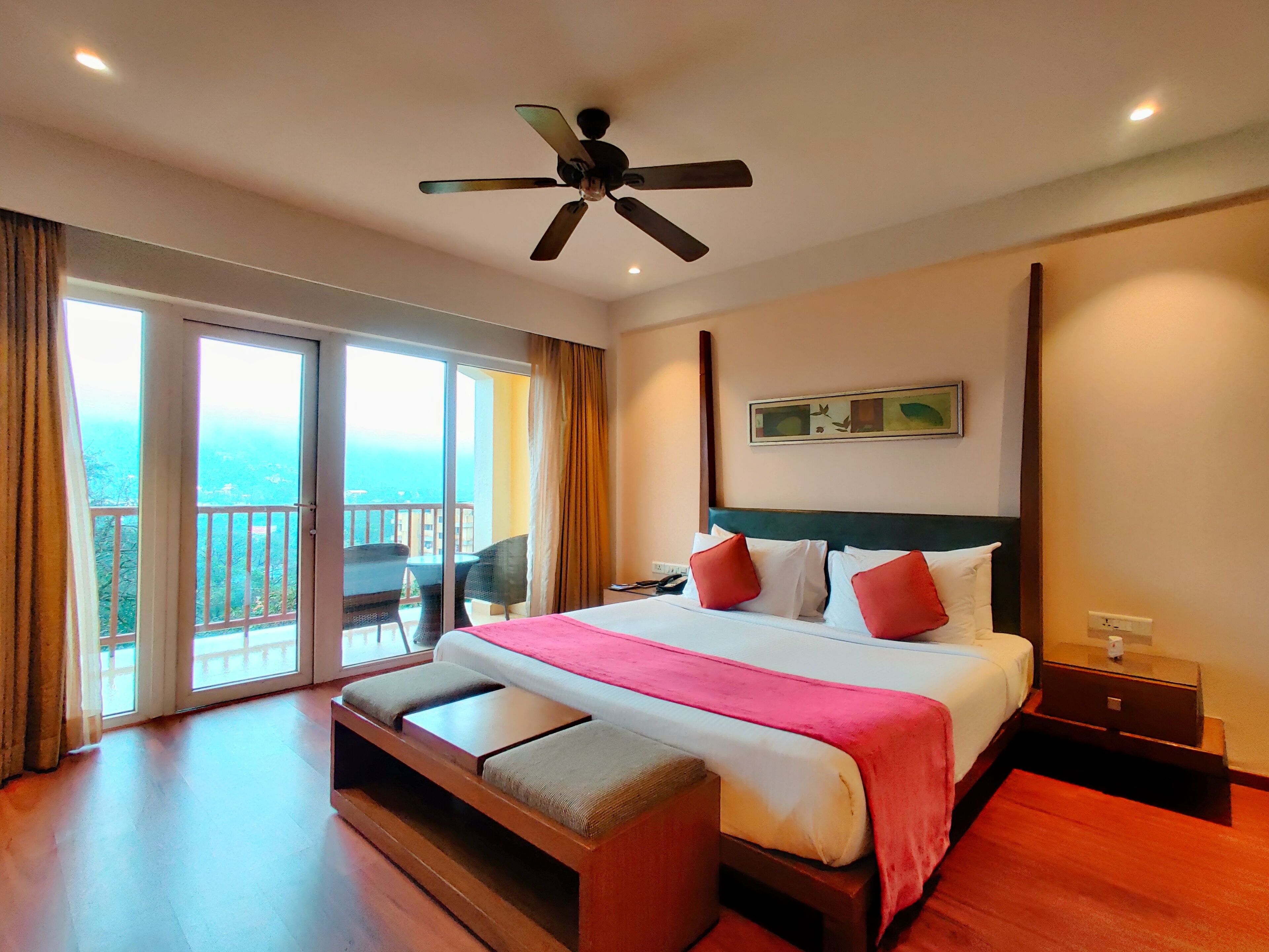 A hotel room with a bed, a bench, a ceiling fan, a nightstand, and a view of the outdoors.