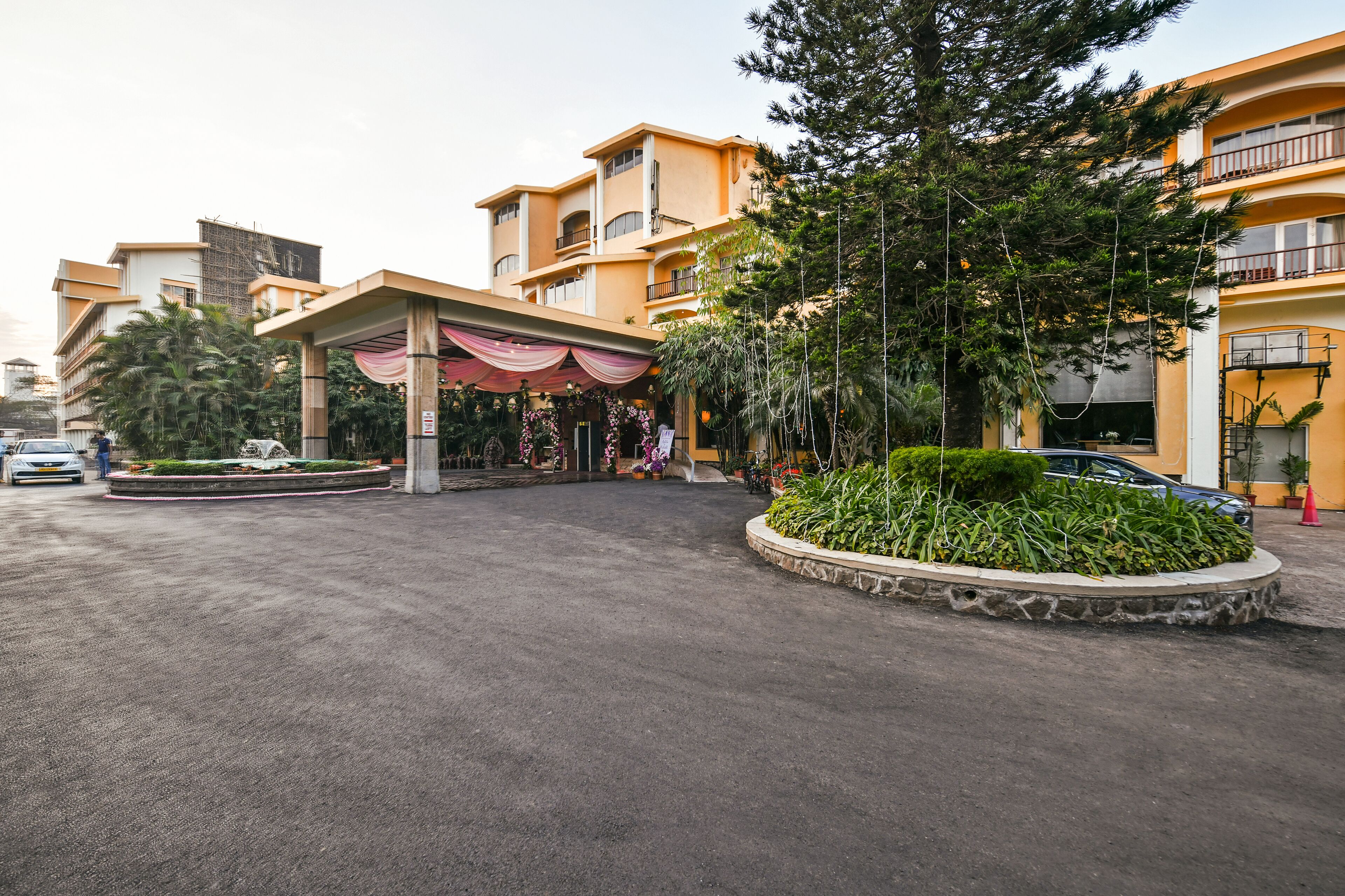 Entrada de hotel con un área techada, jardín ajardinado y un edificio de varios pisos con balcones.