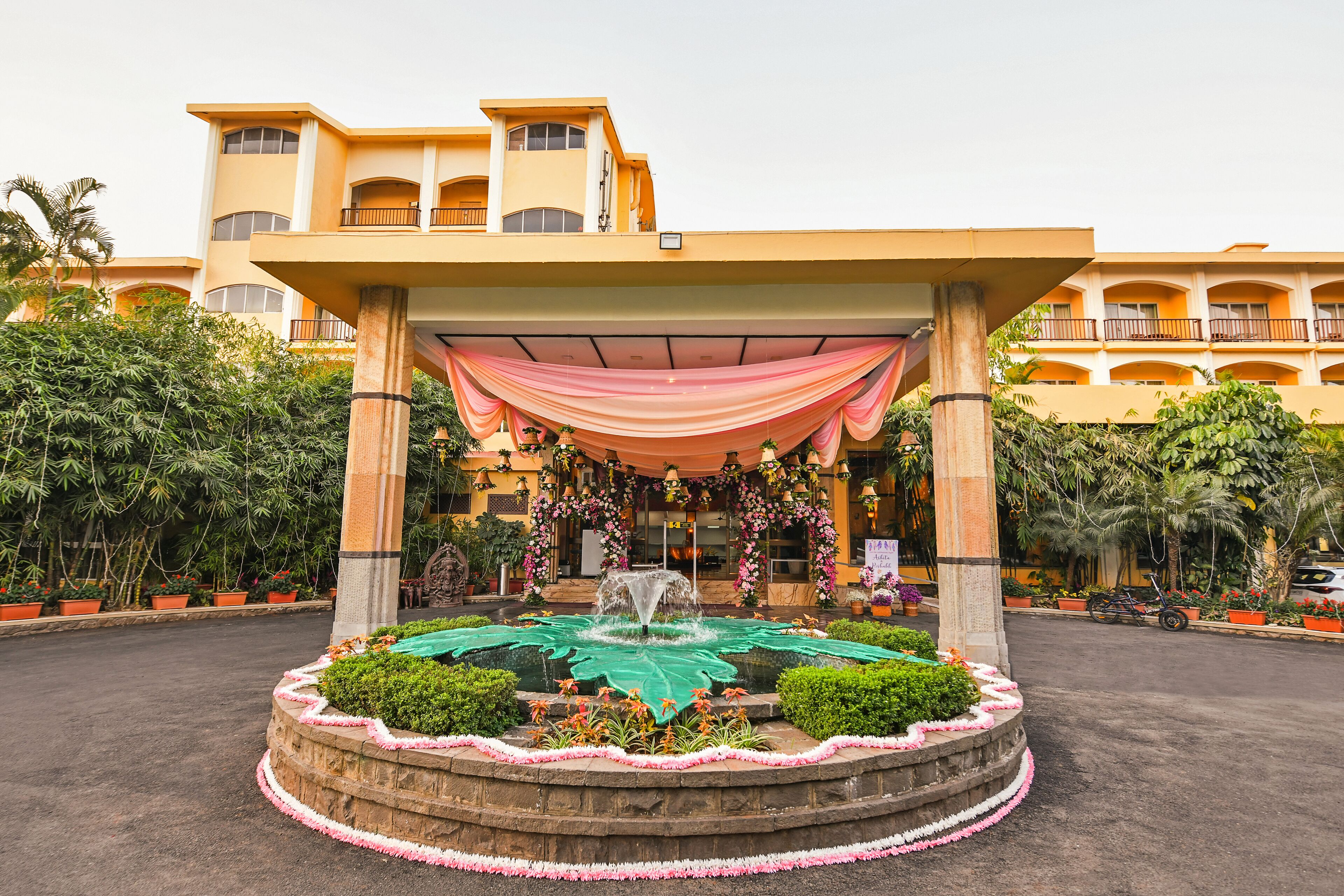 A hotel entrance with a fountain, covered walkway, and lush greenery.