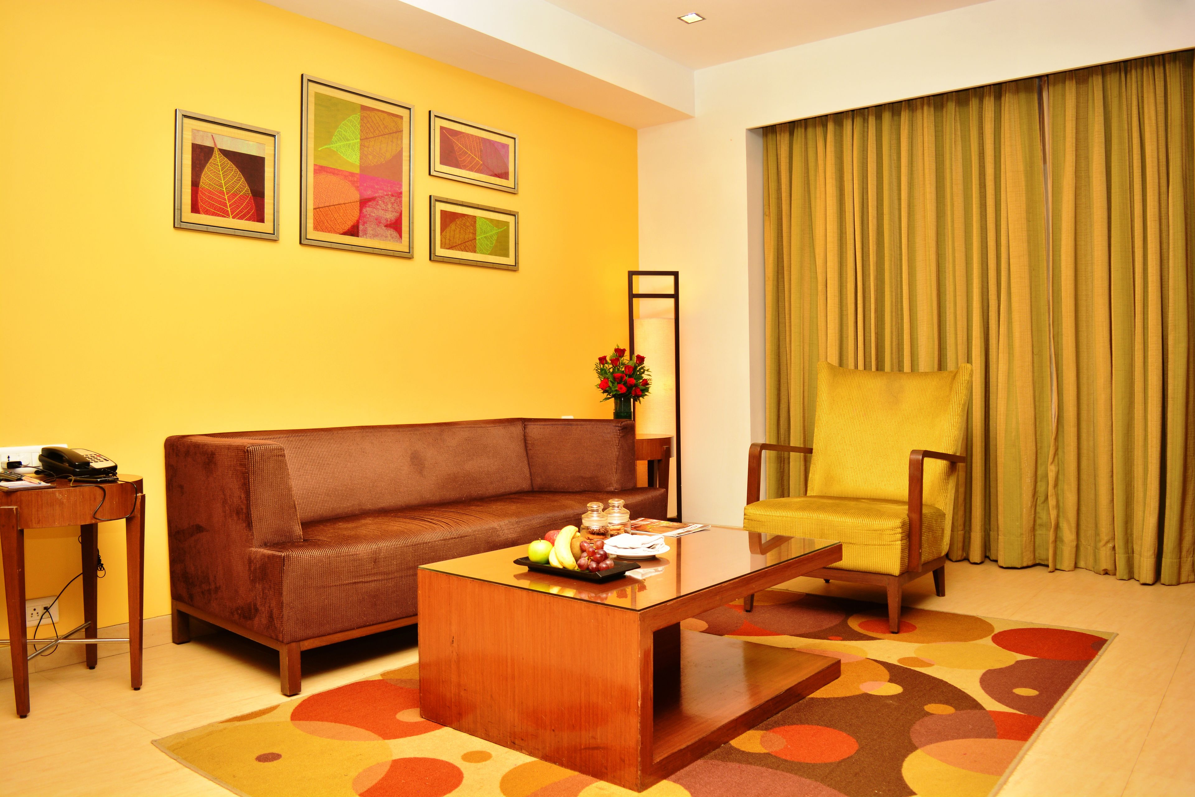A living room with a brown sofa, a yellow armchair, a coffee table, and a small table with a phone and a vase of flowers.