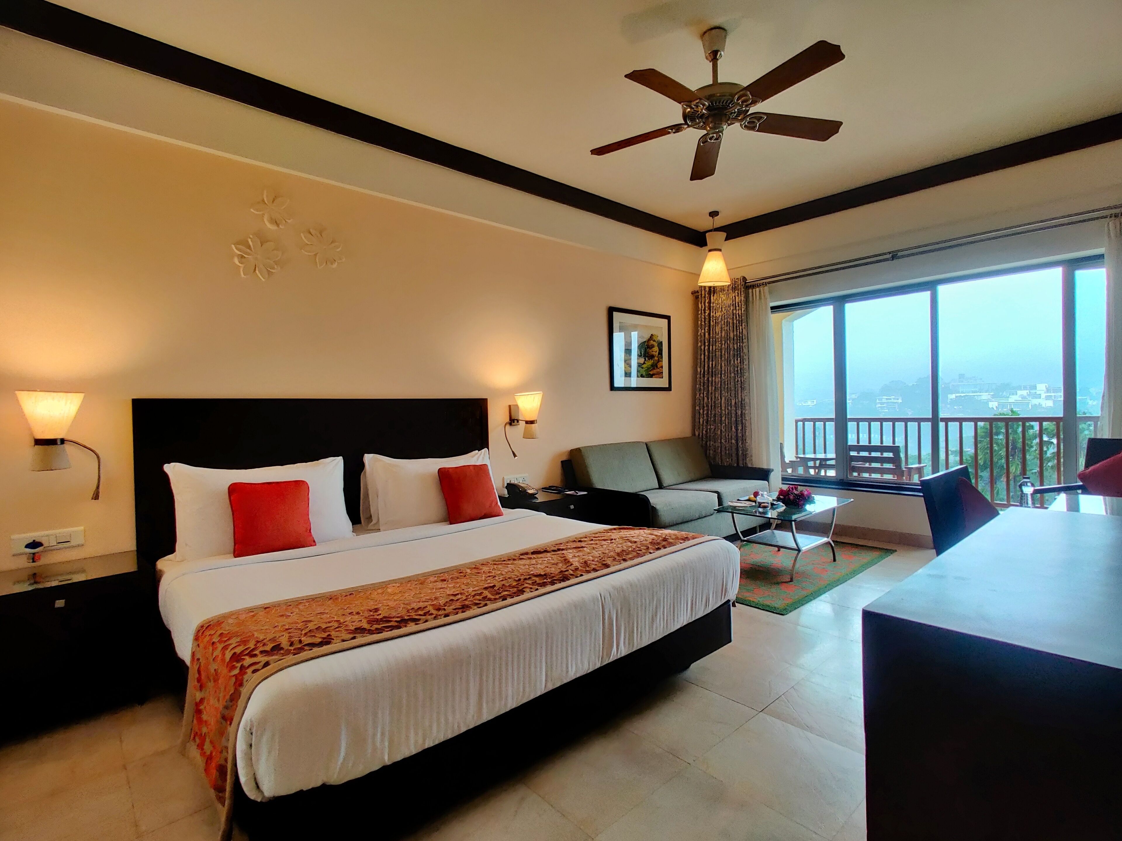 A hotel room with a large bed, a sofa, a dining table, and a balcony with a view.