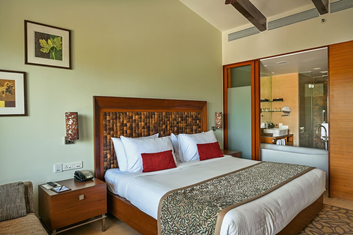 A hotel room with a wooden headboard, a large bed with white and red bedding, a bedside table with a phone and a notepad, and a mirror above the bed.