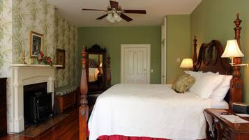 A bedroom with a bed, a wooden dresser, a nightstand, a mirror, a fireplace, and a ceiling fan.