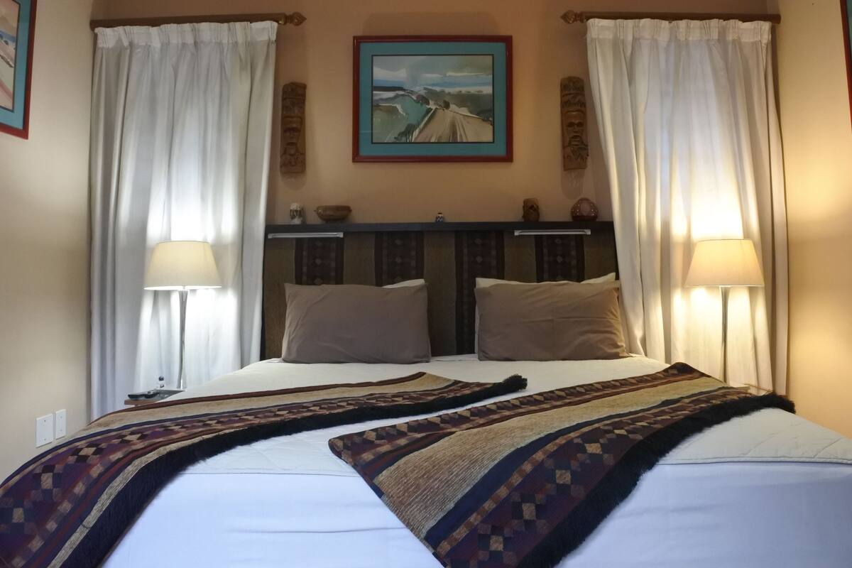 Een hotelkamer met een groot bed, twee bedlampjes, een schilderij aan de muur en een raam met gordijnen.