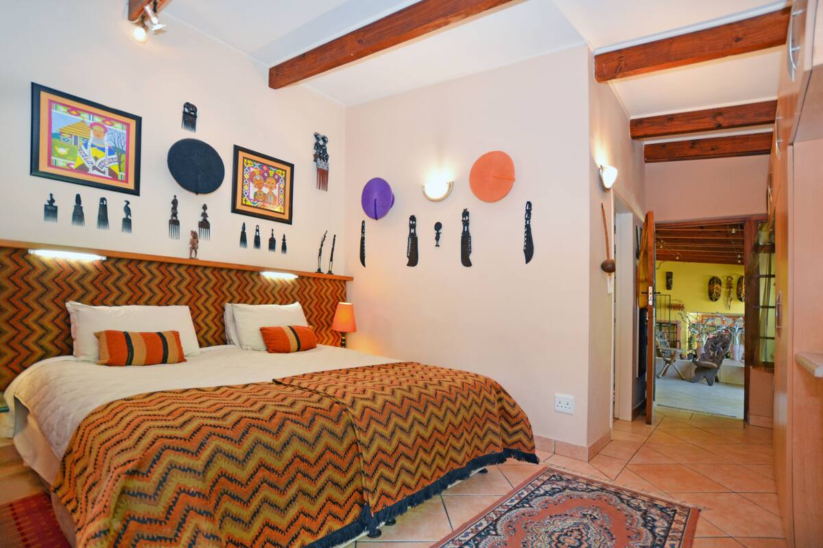 Een slaapkamer met een bed, een wand met decoratieve objecten en een deur naar een andere kamer.