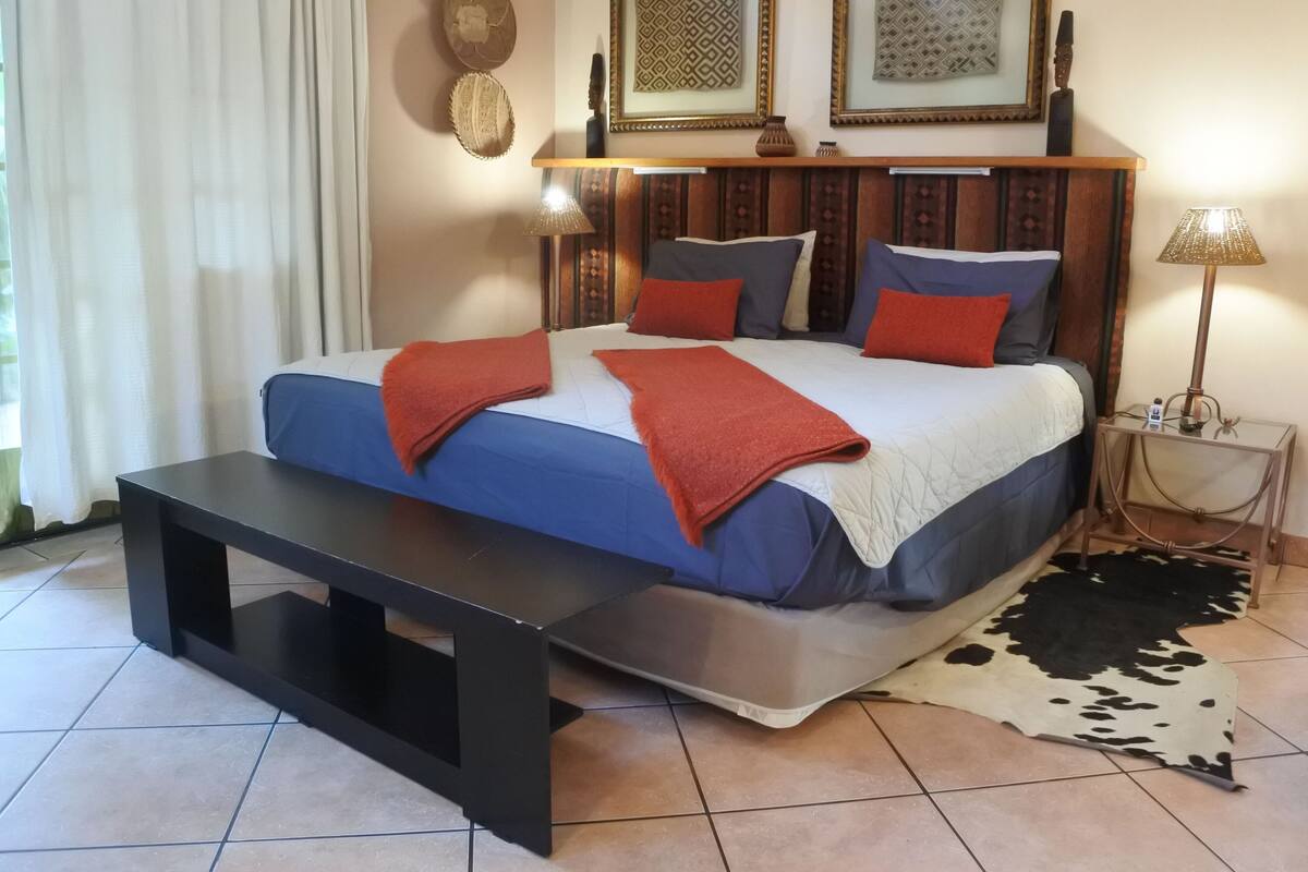 Een slaapkamer met een bed, nachtkastjes, een lamp en een kleden van runderhuid.