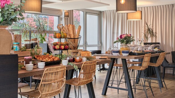 A modern dining area with wicker chairs, a wooden table, and a variety of food items. - The Originals City, Hôtel Le Beaujoire, Nantes (Nantes)
