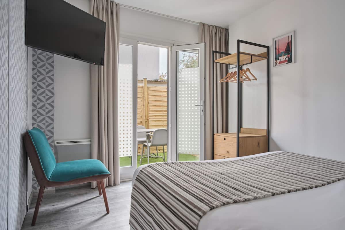 A bedroom with a bed, a chair, a wardrobe, and a sliding glass door leading to an outdoor area.