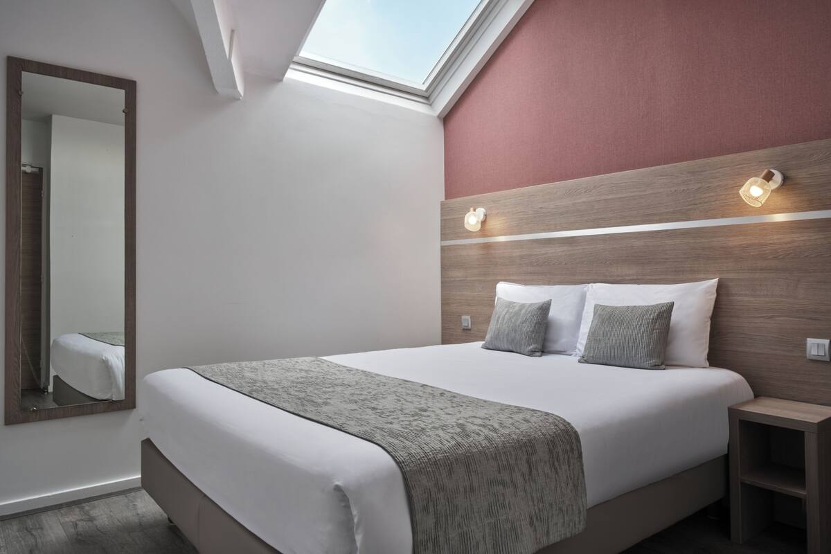 A modern hotel room with a skylight, a large bed, a wooden headboard, and a nightstand.