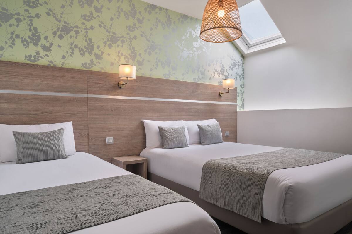 A hotel room with two beds, a wooden headboard, wall-mounted lights, and a skylight.