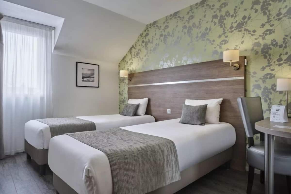 A hotel room with two beds, a desk, and a chair.