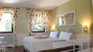 Un dormitorio con cama, mesitas de noche, una ventana con cortinas, un espejo y un radiador.