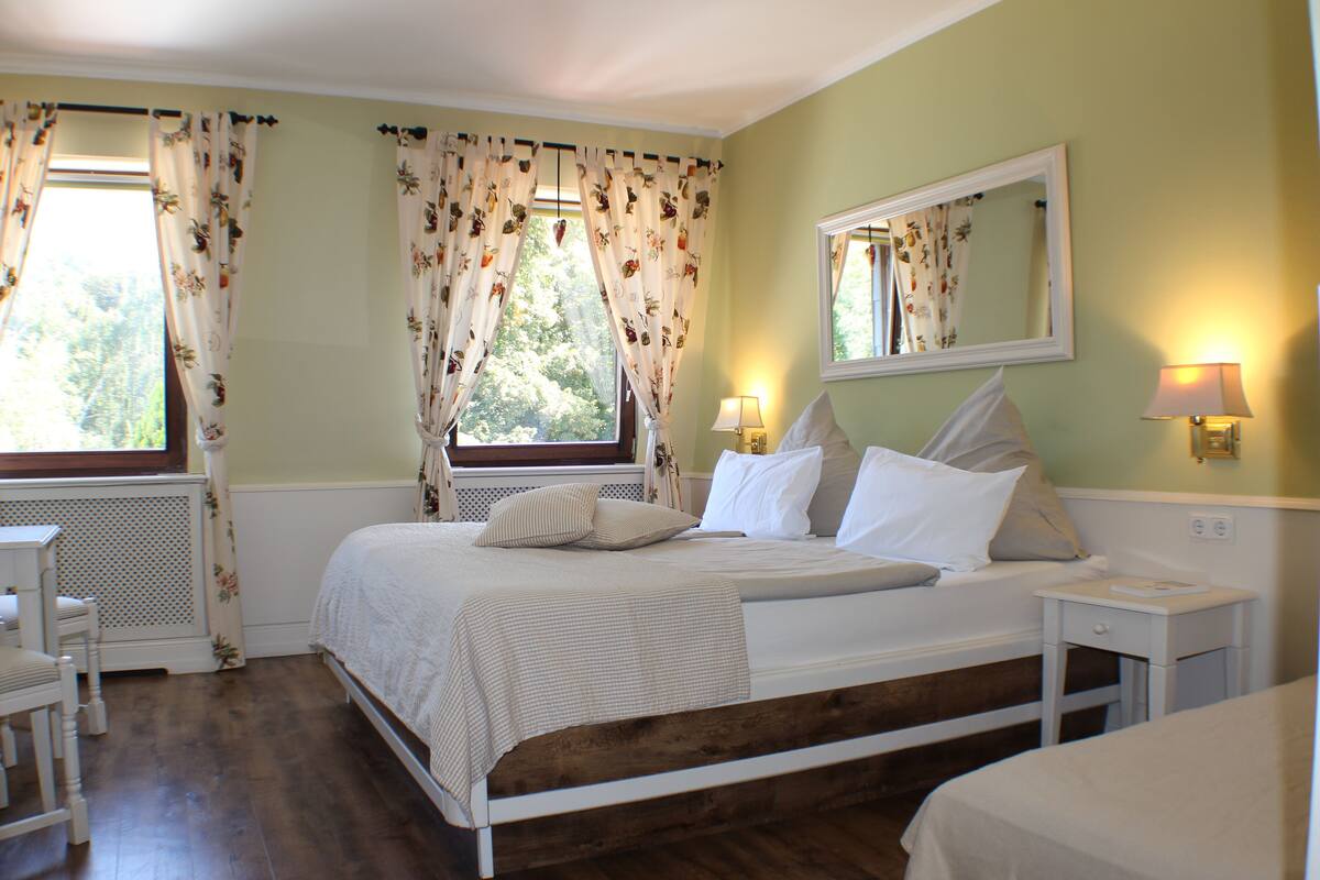 A bedroom with a bed, bedside tables, a window with curtains, a mirror, and a radiator.