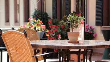 Une table ronde en bois, entourée de chaises en osier, un pot de fleurs et une fenêtre avec des volets.