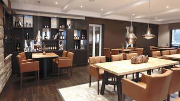 A modern dining area with wooden tables and leather chairs, a bar with shelves of bottles, and pendant lighting.