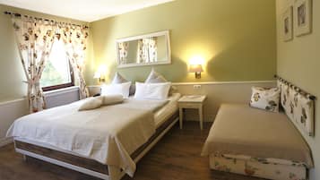 Een slaapkamer met een groot bed, een kleiner bed, een nachtkastje, een spiegel en een raam met gordijnen.