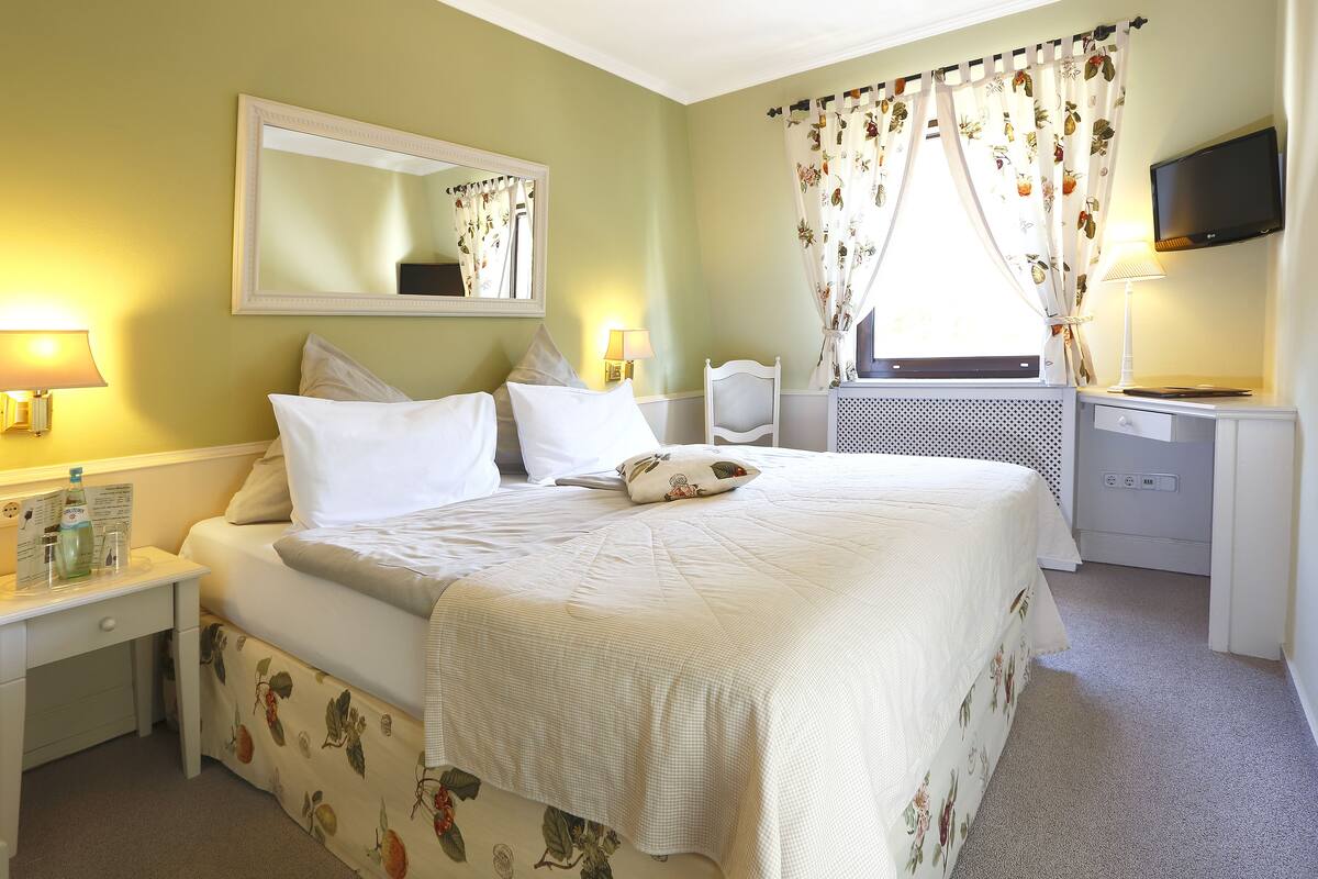 A neatly arranged hotel room with a bed, bedside tables, a desk, and a television.