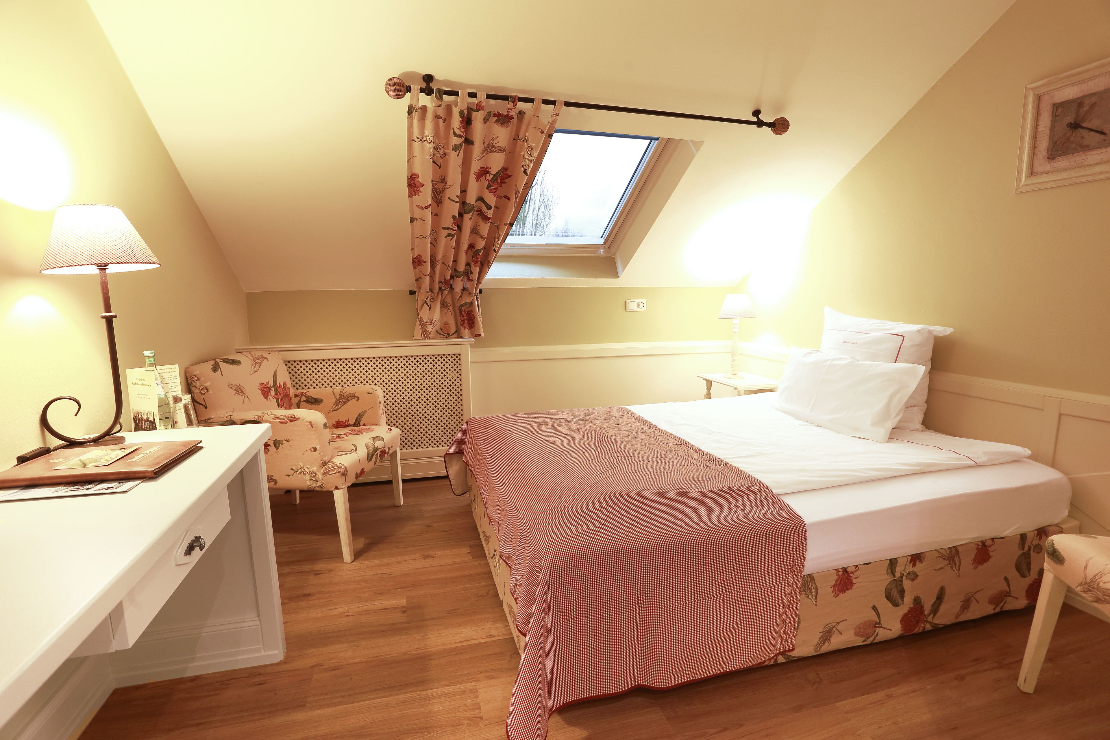 A bedroom with a bed, a desk, a chair, a window with curtains, and a radiator.