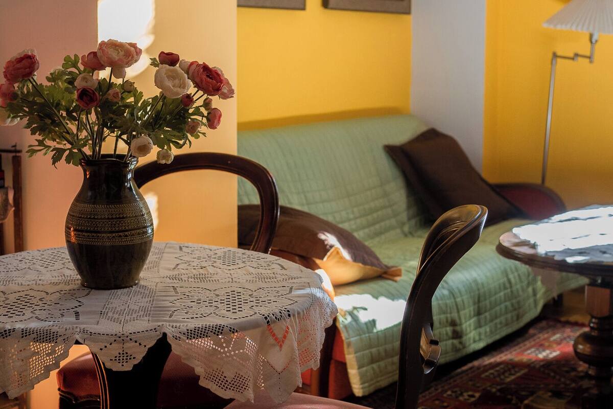 A dining area with a table set for four, a vase with flowers, and a green sofa in the background.
