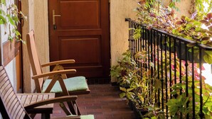 A wooden door with a number plate, a brick pathway, and a metal railing with plants. - Kolory Guest House (Kraków)