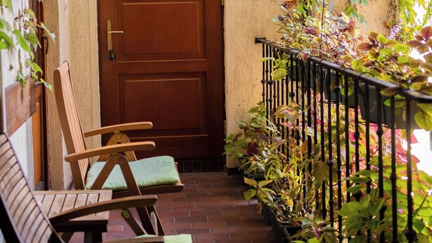 A wooden door with a number plate, a brick pathway, and a metal railing with plants. - Kolory Guest House (Kraków)