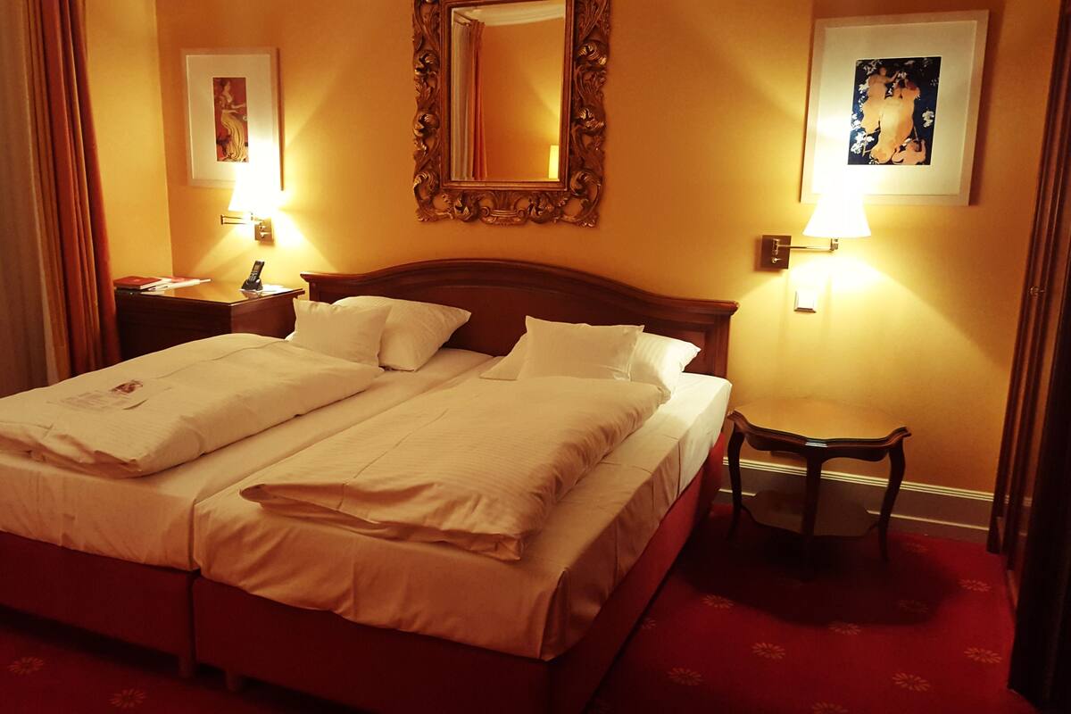 A hotel room with a double bed, two bedside tables, a nightstand, a mirror, and two wall-mounted lamps.