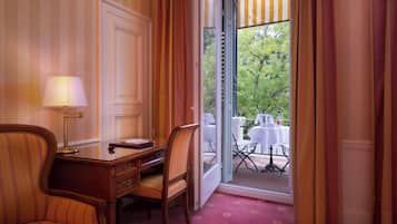 A hotel room with a desk, two chairs, a lamp, and a view of an outdoor dining area.