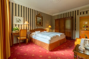 Habitación de hotel con una cama grande, un escritorio con una silla, un aparador y un espejo en la pared.