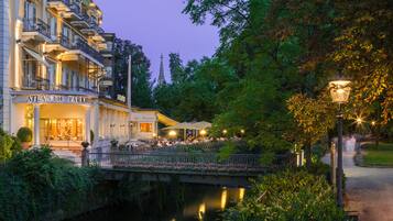 The exterior of the Atlantic Park Hotel with a cafe, a bridge over a canal, and surrounding greenery.