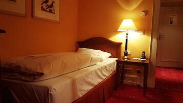 Quarto de hotel com cama, mesa de cabeceira com abajur, telefone e porta.
