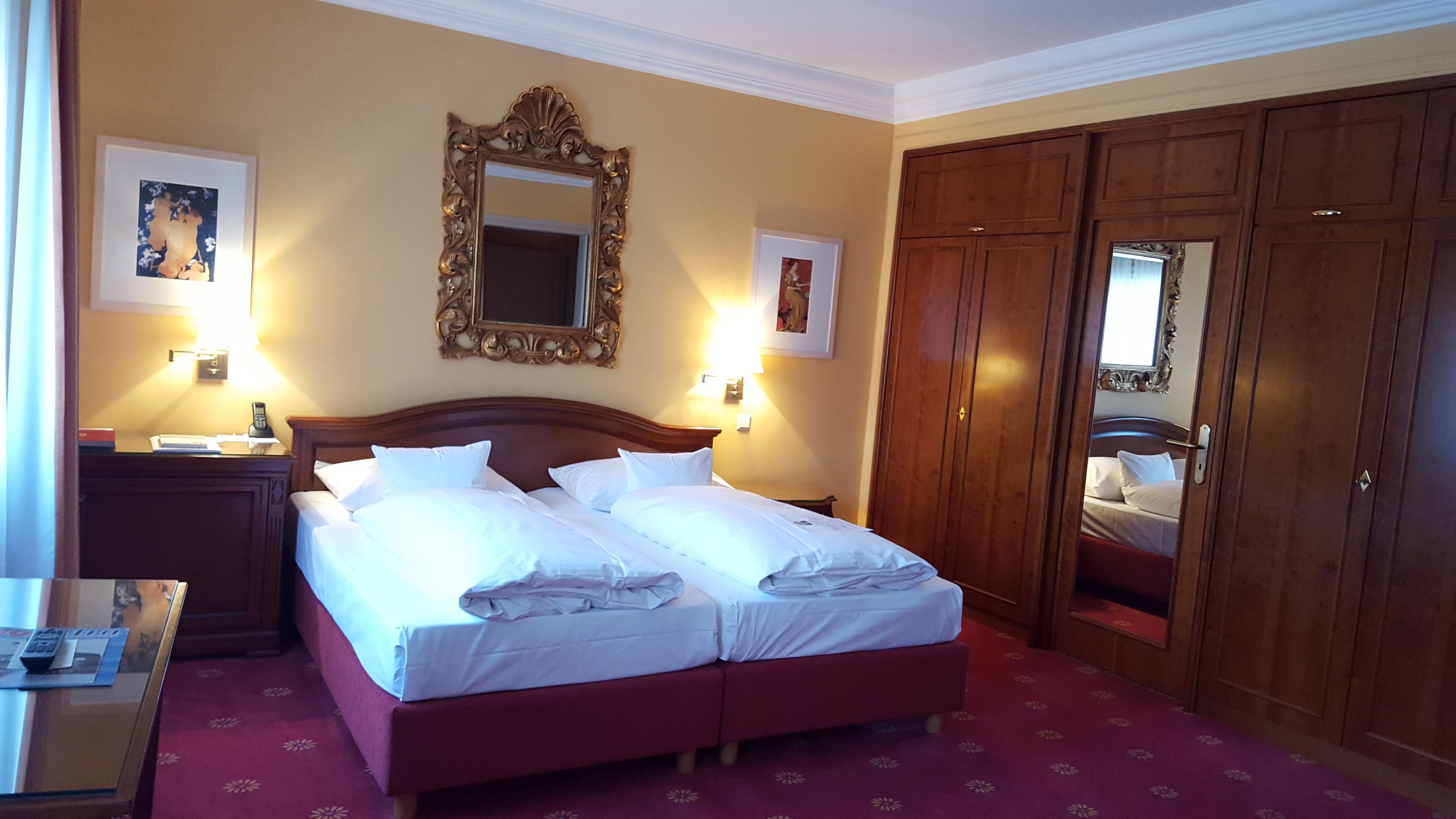 A double bed with white linens, a wooden headboard, two bedside lamps, and a large mirror above the bed.