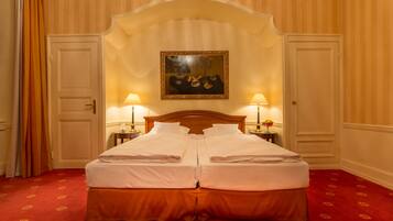 A double bed with a wooden headboard, two bedside tables with lamps, a painting above the bed, and a red carpeted floor.
